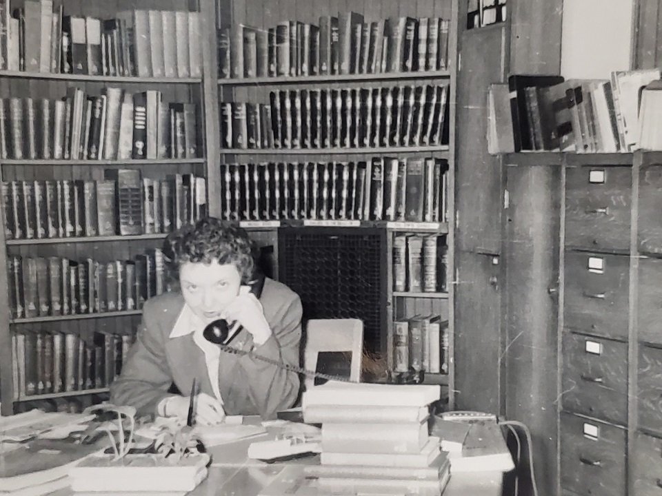 Black and white photo of a staff member answering a phone in front of books.