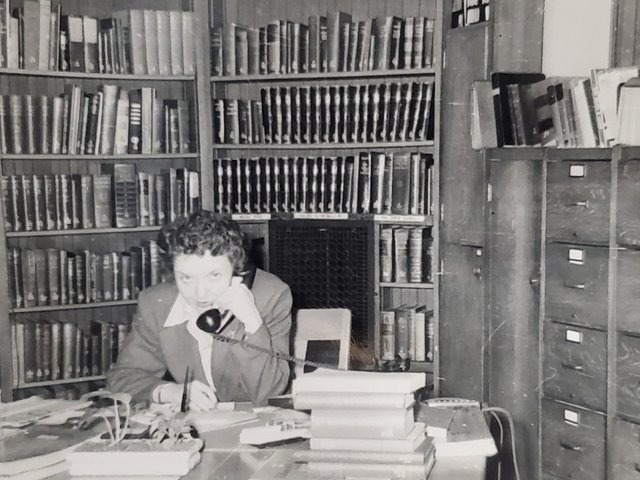 Black and white photo of a staff member answering a phone in front of books.