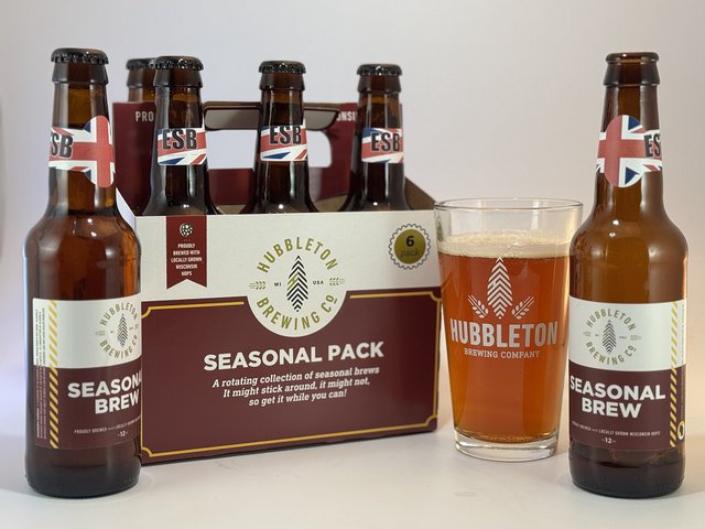 A six-pack of bottles plus a poured pint glass of an amber beer from Hubbleton brewing.