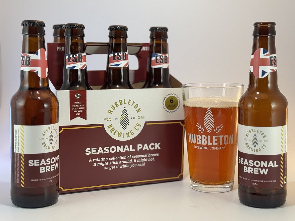 A six-pack of bottles plus a poured pint glass of an amber beer from Hubbleton brewing.