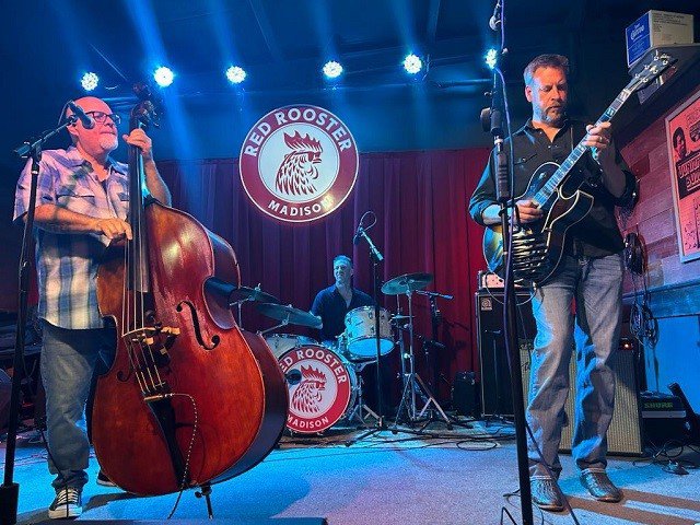 A three-piece band on stage at the Red Rooster.