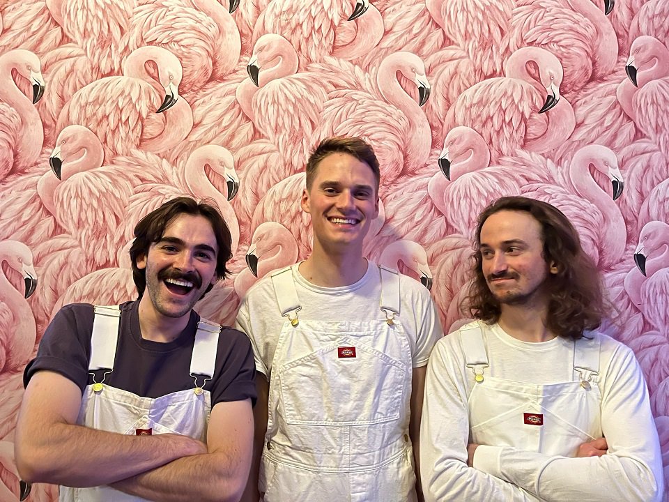 A close-up of The Night Painters in front of a mural of flamingos.