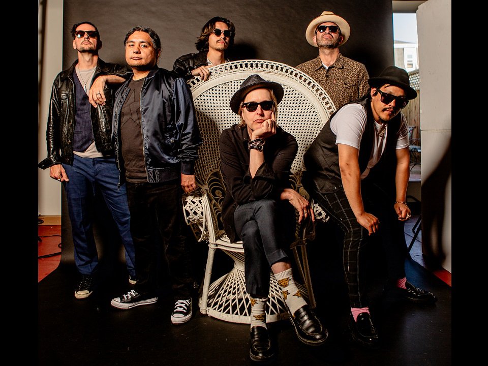 The members of Cumbia Shoes gathered around a seated Chuck Prophet.