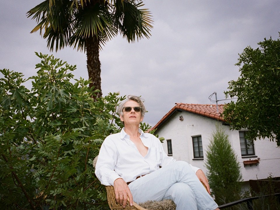 Dean Wareham sitting outside in front of a palm tree.