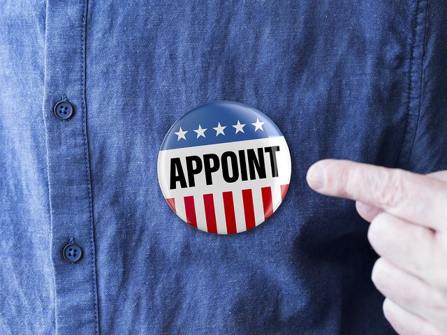 A man wearing a pin on his shirt that says "appoint."