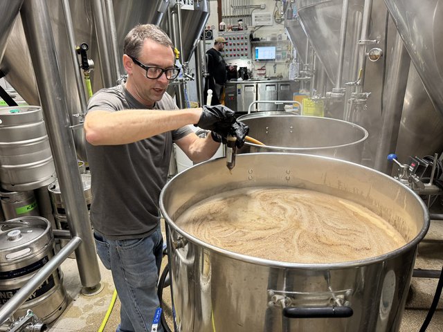 A man in a brewery with a big vat of beer.