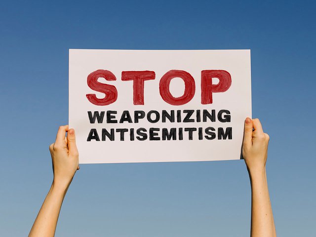 A person holding a protest sign saying "Stop weaponizing antisem