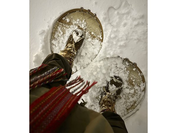 A downward view of a person wearing snowshoes.