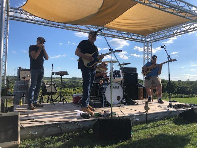 A three-piece band on an outdoor stage.